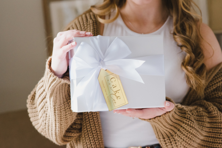 A woman holding up a white gift box with a white bow and gold tag