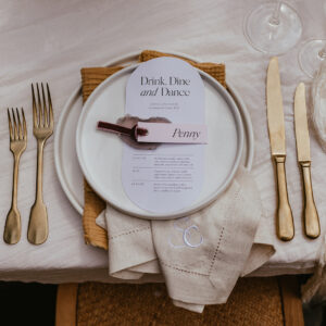 A wedding place setting featuring gold cutlery on either side of a plate that is resting on an embroidered napkin