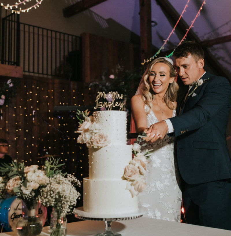 A couple cutting their wedding cake, featuring a laser cut lettering cake topper